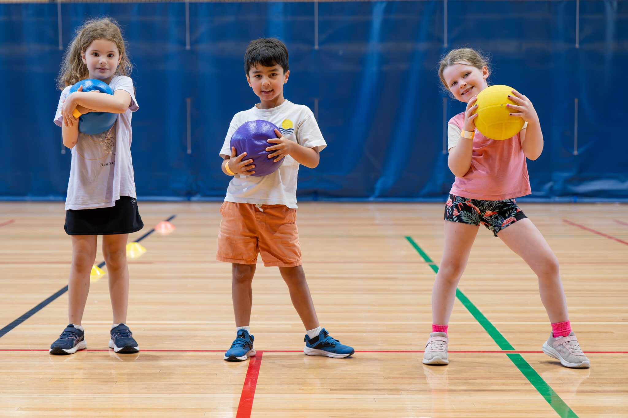 Three children holding dodgeballs and posing for the camera