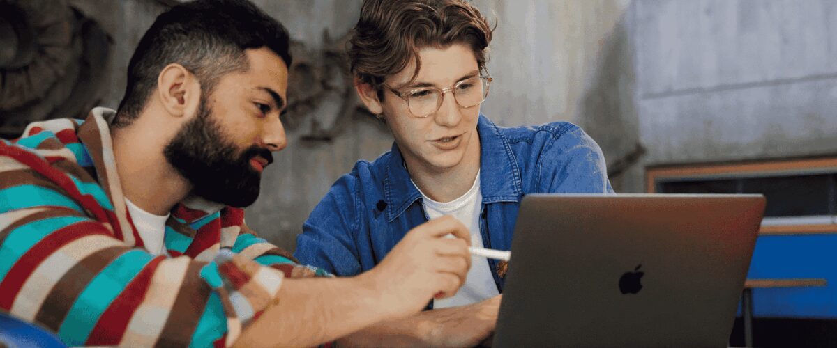 Two people working together at a table, looking at a laptop.