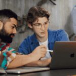 Two people working together at a table, looking at a laptop.