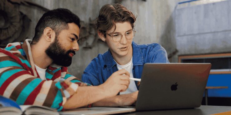 Two people working together at a table, looking at a laptop.