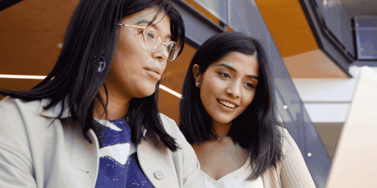 Two people working together at a table, looking at a laptop.