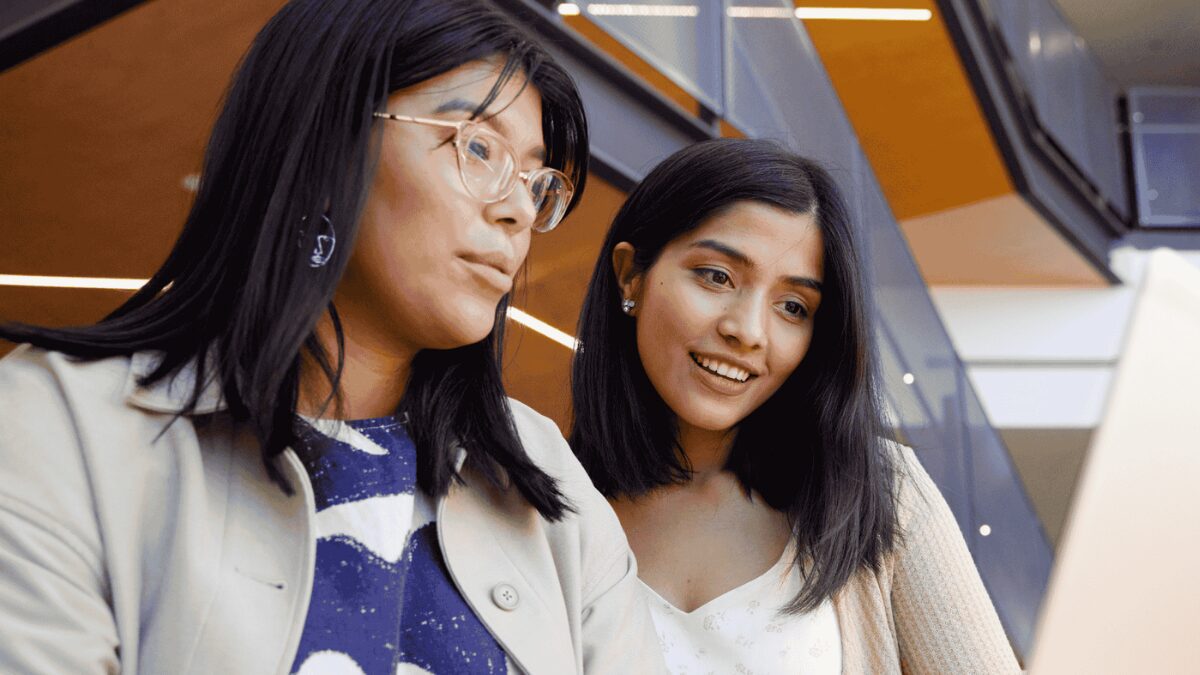 Two people working together at a table, looking at a laptop.