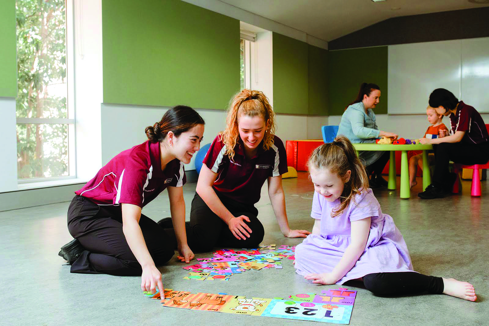 Two female student occupational therapists sit on the floor with a young child playing a card game.