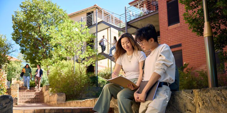 Curtin students smiling looking at documents outside accommodation.