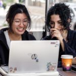 Two people working on laptops at an outdoor table with a coffee cup