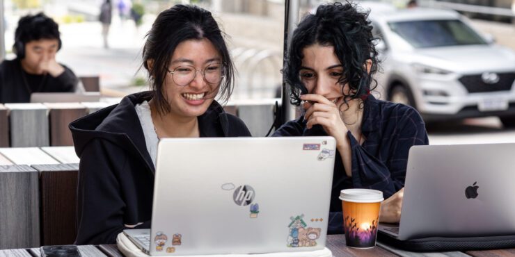 Two people working on laptops at an outdoor table with a coffee cup