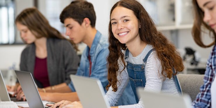 Portrait of smiling university student sitting in a row with classmates, who are all studying together on laptops.