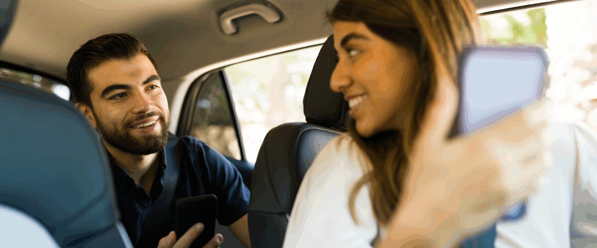 Happy people in the driver and passenger seat of a car looking at their phones.
