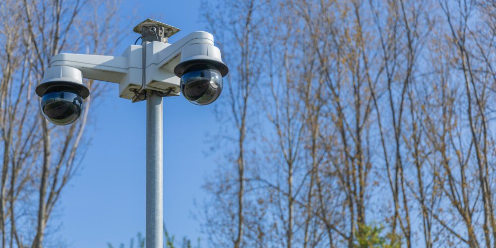 Two security cameras are mounted on a pole, watching over the area under a clear sky