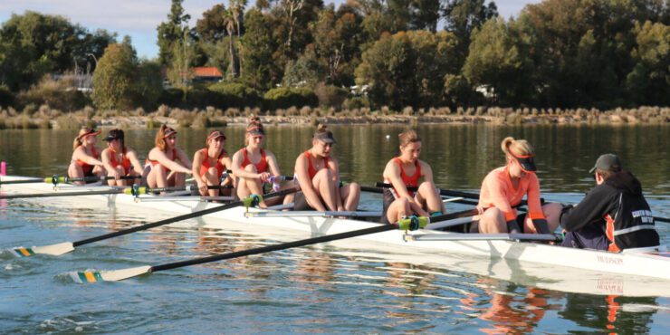 Students rowing together on calm water during a beginner rowing session at Curtin.