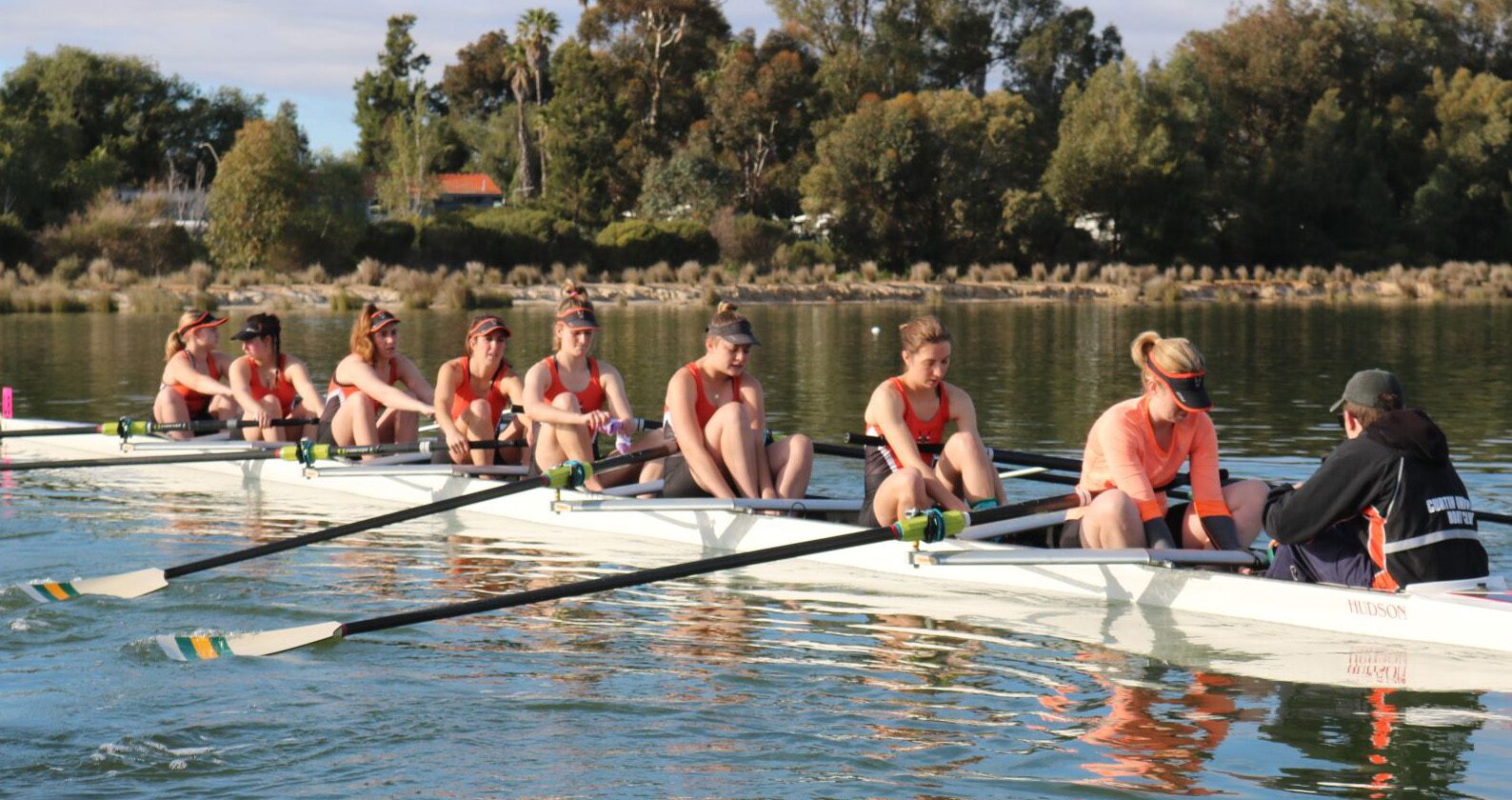 Students rowing together on calm water during a beginner rowing session at Curtin.