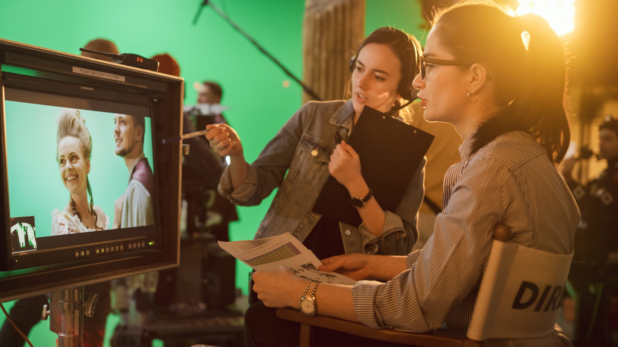 Female Director in Chair Looks at Display talks with Assistant, Shooting Blockbuster. Green Screen Scene