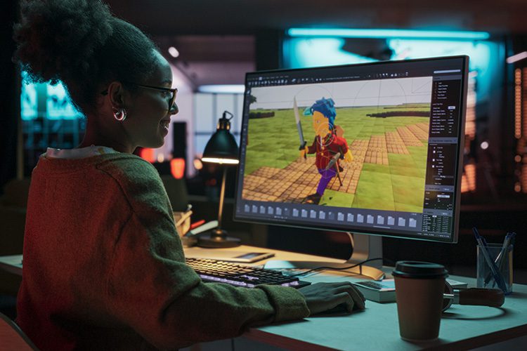 Portrait of African American female video game designer creating a video game character on laptop in an office at at night.