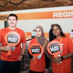 Three students wearing orange t-shirts and holding West Tech signs.