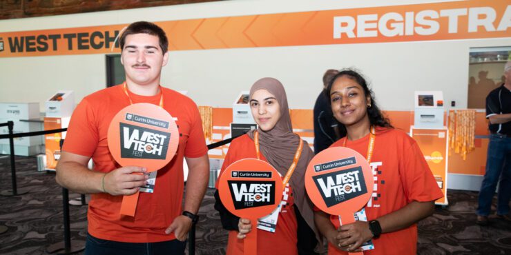Three students wearing orange t-shirts and holding West Tech signs.
