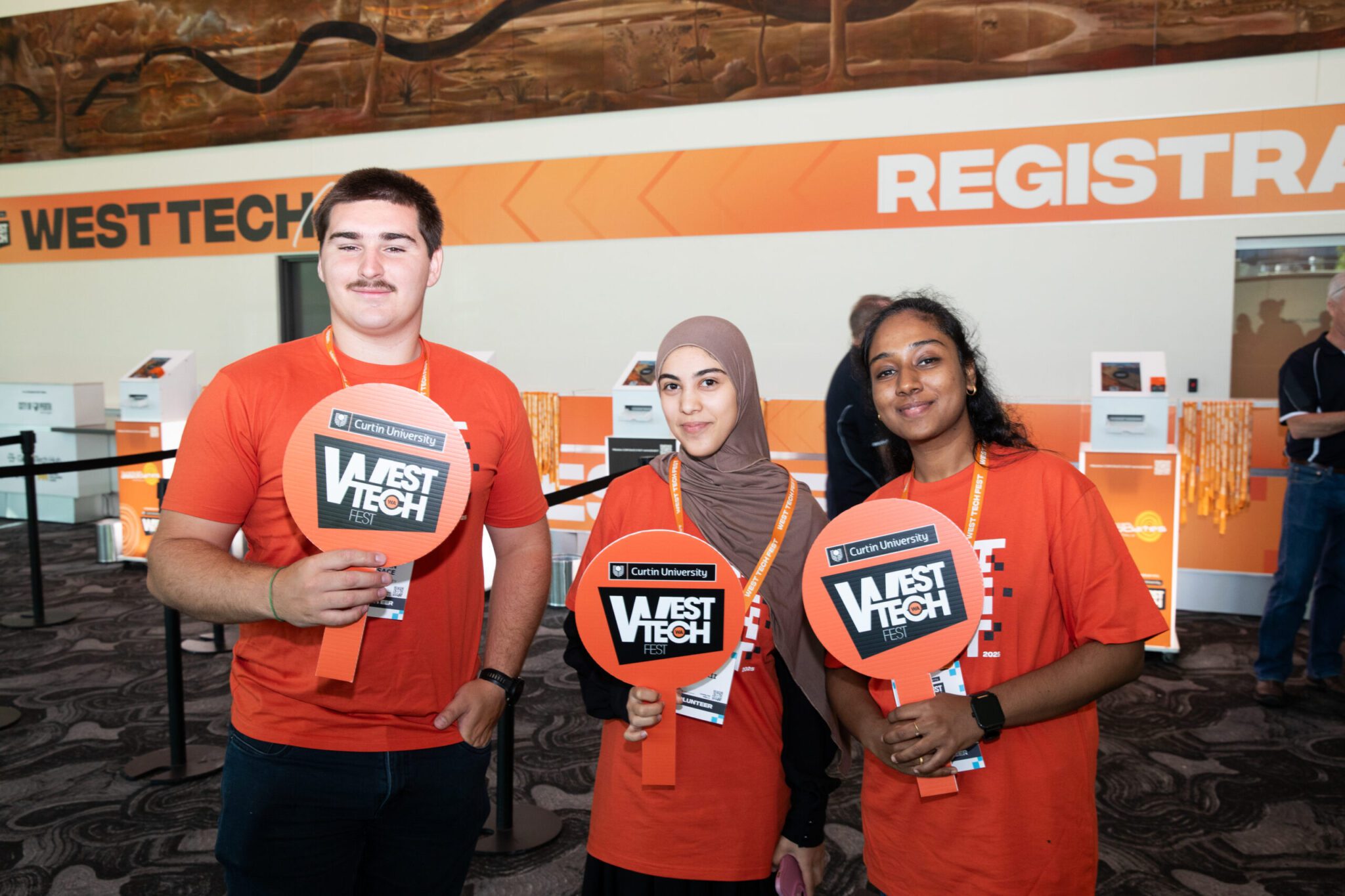 Three students wearing orange t-shirts and holding West Tech signs.