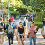 Students walking along a leafy campus pathway with backpacks on a sunny day