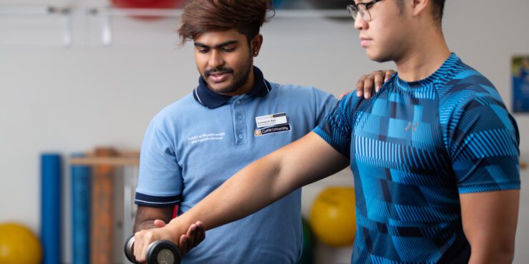 Physiotherapy student guiding a client through an arm strength exercise with a dumbbell in a clinic setting.
