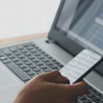 A person using a smartphone alongside a laptop showing a sign‑in screen.