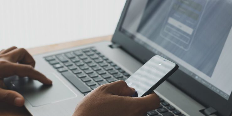 A person using a smartphone alongside a laptop showing a sign‑in screen.