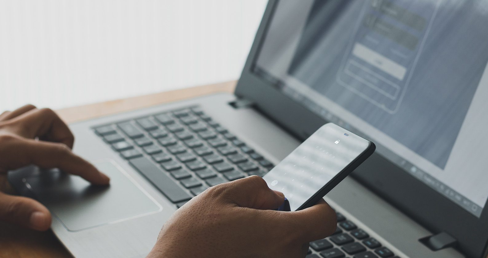 A person using a smartphone alongside a laptop showing a sign‑in screen.