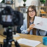 Business woman in glasses recording presentation on camera.