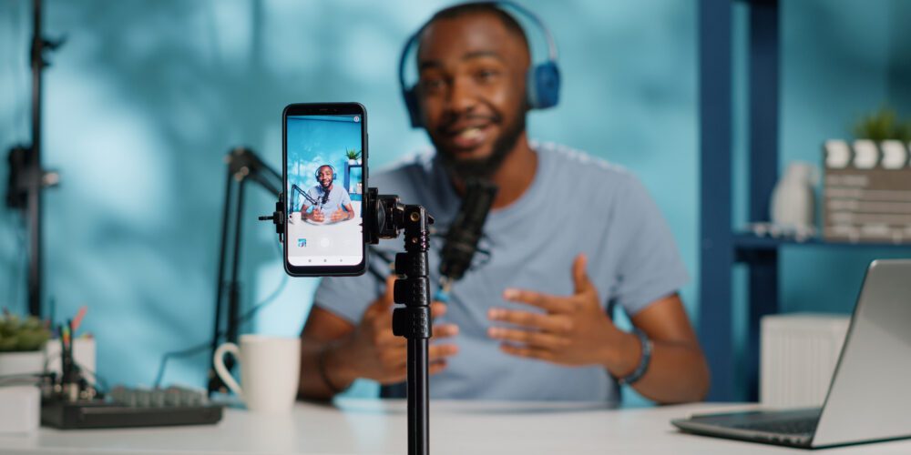 Close up of blogger filming video with smartphone on tripod for online vlog. Content creator using mobile phone and videography equipment to record for podcast channel on social media.