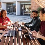 Students working together outdoors with laptops at campus seating.