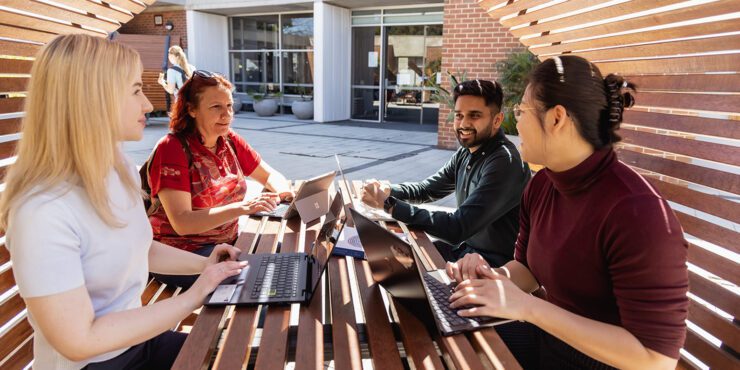 Students working together outdoors with laptops at campus seating.