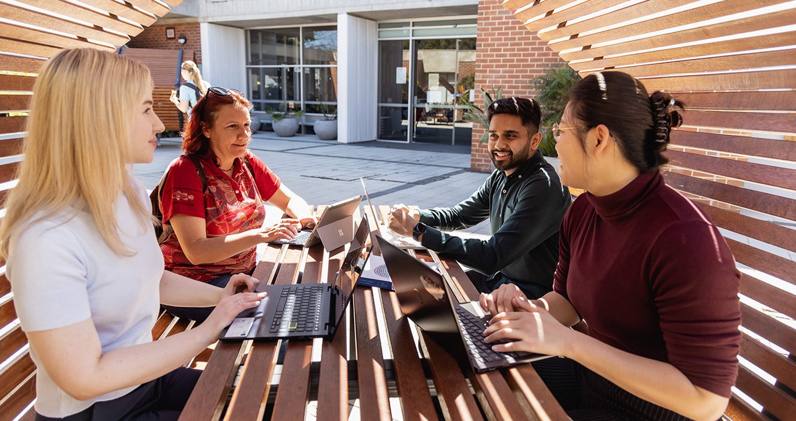 Students working together outdoors with laptops at campus seating.