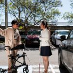Two people talking in a car park, one using a mobility walker.
