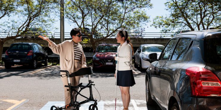 Two people talking in a car park, one using a mobility walker.