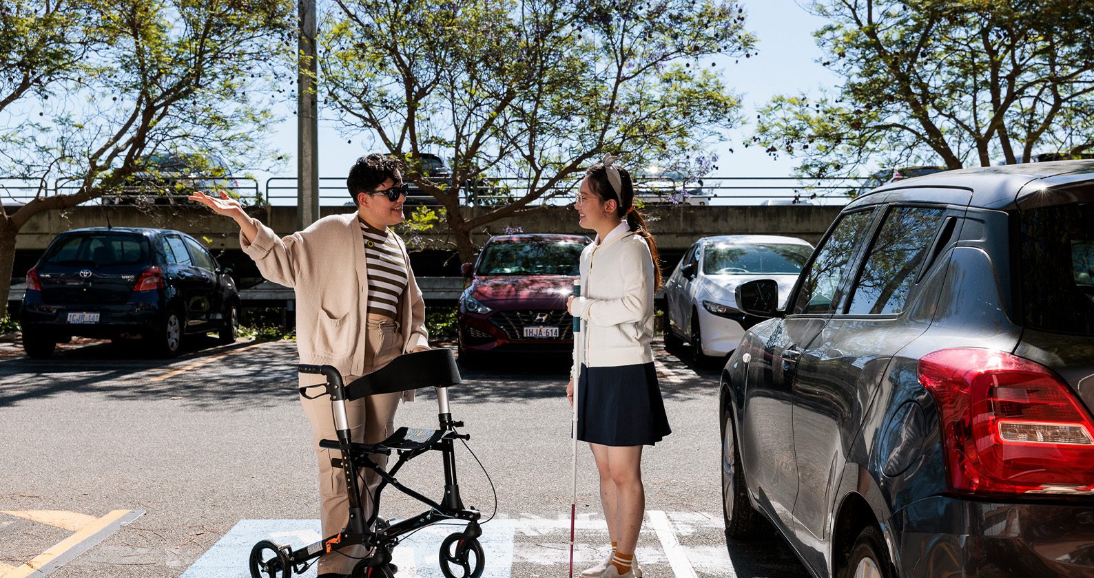 Two people talking in a car park, one using a mobility walker.
