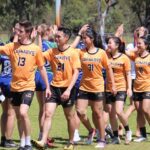 Curtin students in team uniforms walking together on a grass field during a university sports competition.