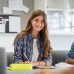 Portrait of happy young woman writing notes and looking at camera.