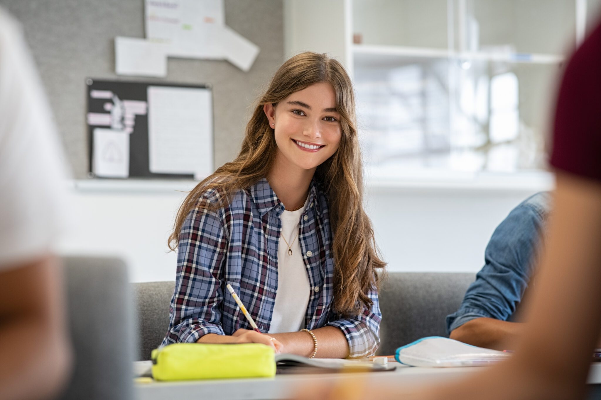 Portrait of happy young woman writing notes and looking at camera.