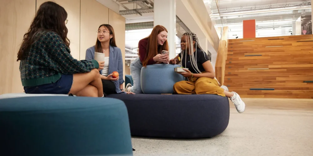 Four students in TL Robertson Library casually talking in groups of two. 