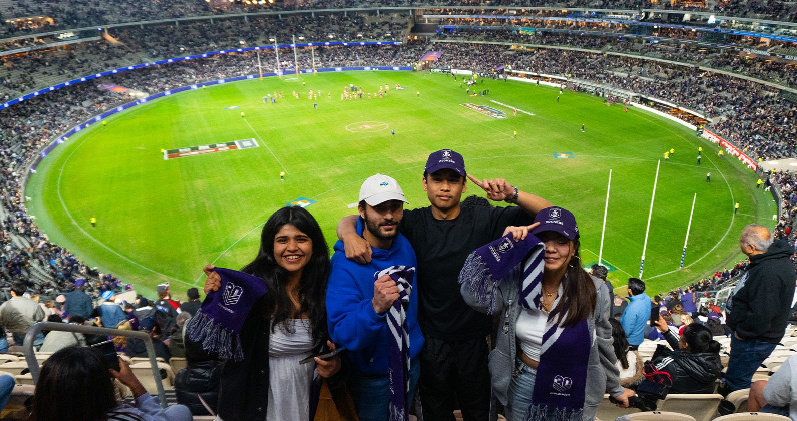 Four people standing in a stadium holding Dockers scarves with a football field and crowd in the background. Provide your feedback on BizChat