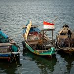 Traditional fishing boats docked at Jakarta harbor with Indonesian flag.