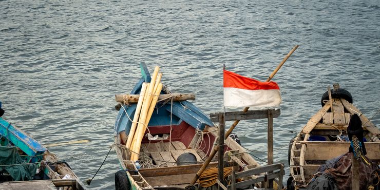 Traditional fishing boats docked at Jakarta harbor with Indonesian flag.