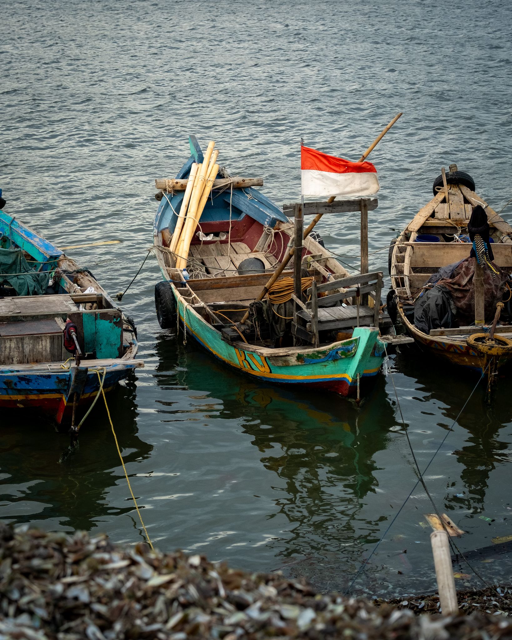 Traditional fishing boats docked at Jakarta harbor with Indonesian flag.