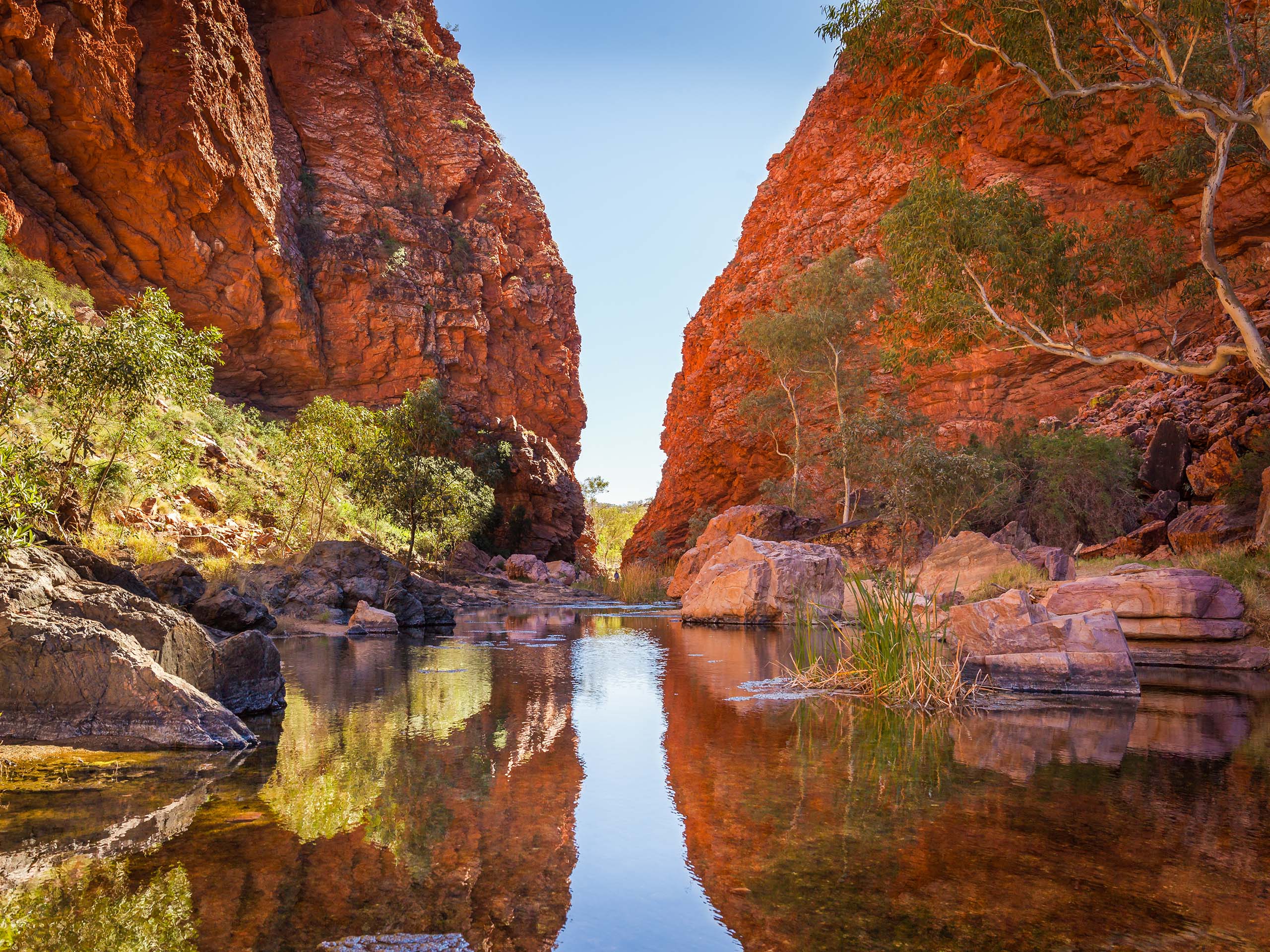 Picturesque view of the Australian outback, with large red natural rock structures, trees and water