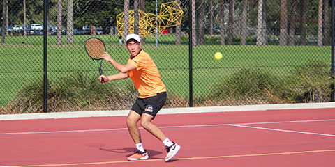 Male student hits a tennis ball with a racquet