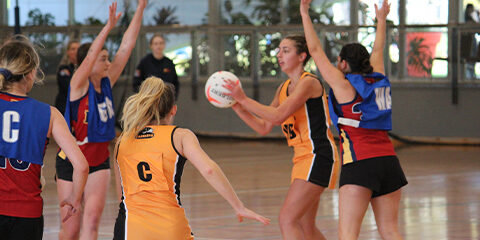 Student wearing an orange netball jersey throwing a netball