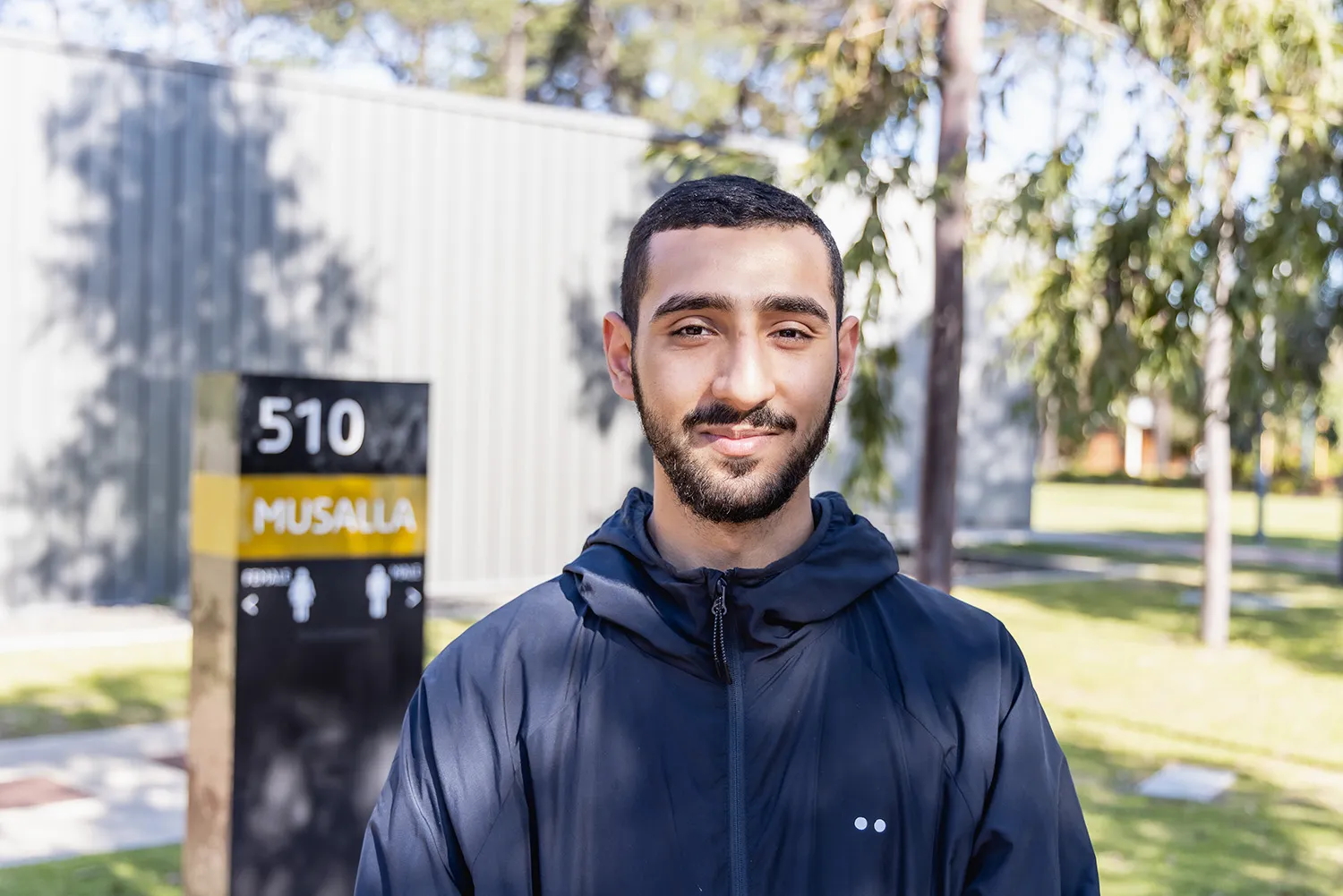 A Muslim male student smiling in front of the Musalla