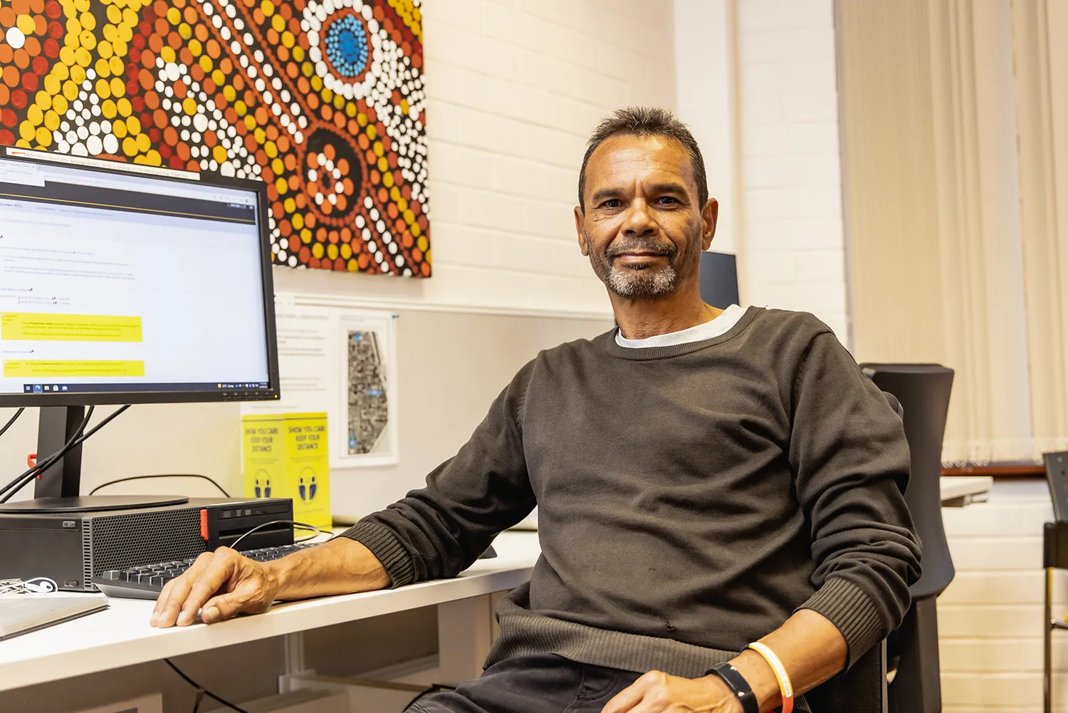 An Indigenous student sitting in front of a computer smiling at the camera