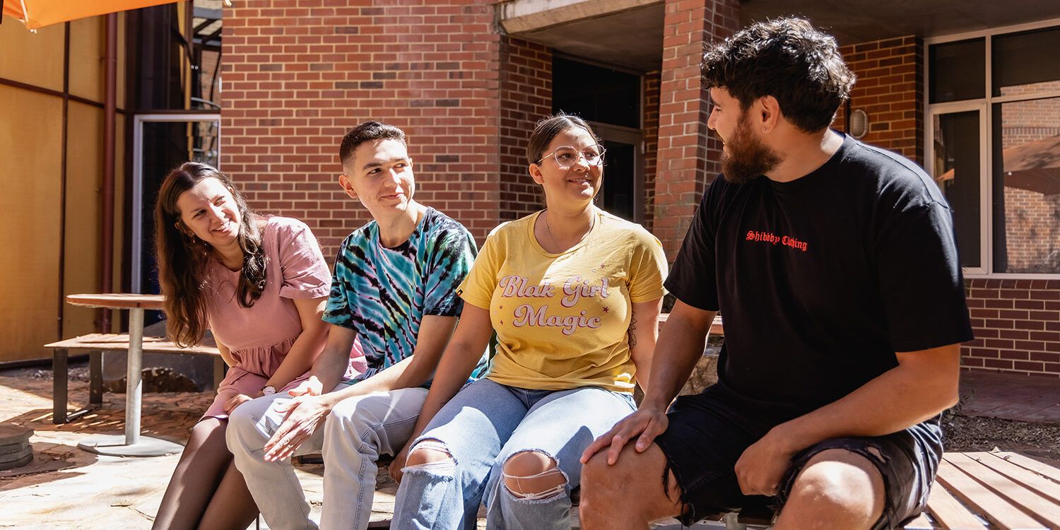 4 students sitting at a bench looking at each other and smiling