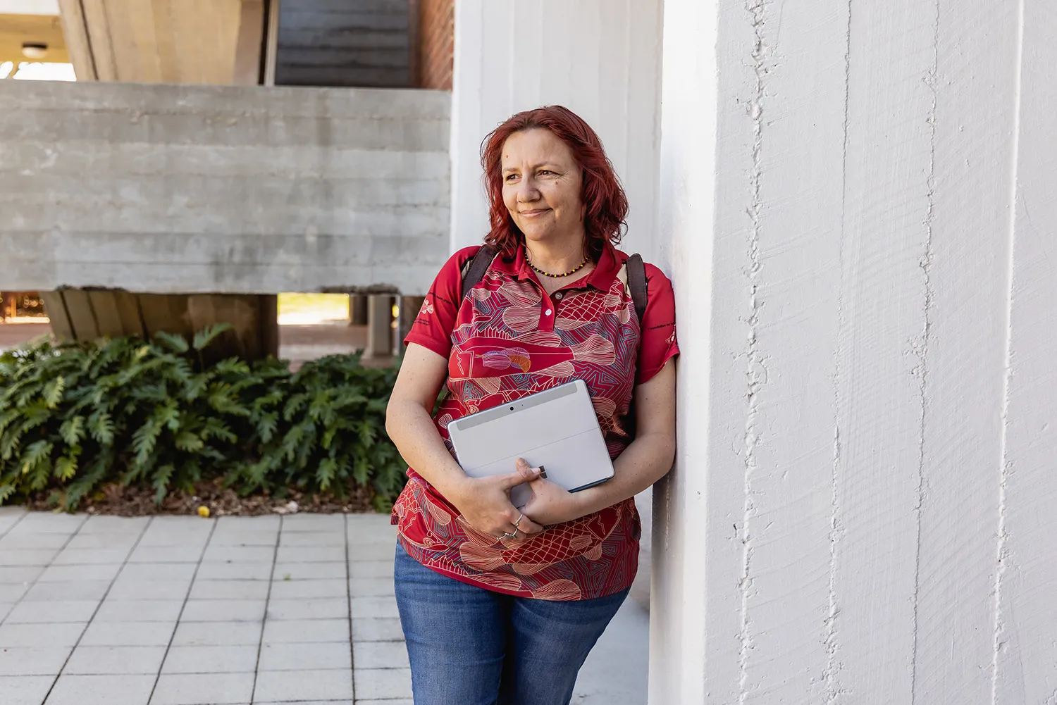 An Indigenous student holding a laptop leaning against the wall