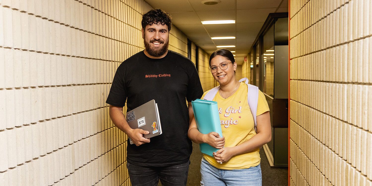 Two students standing in hallway smiling at camera