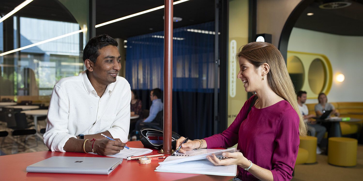 2 students helping each other with work at a table